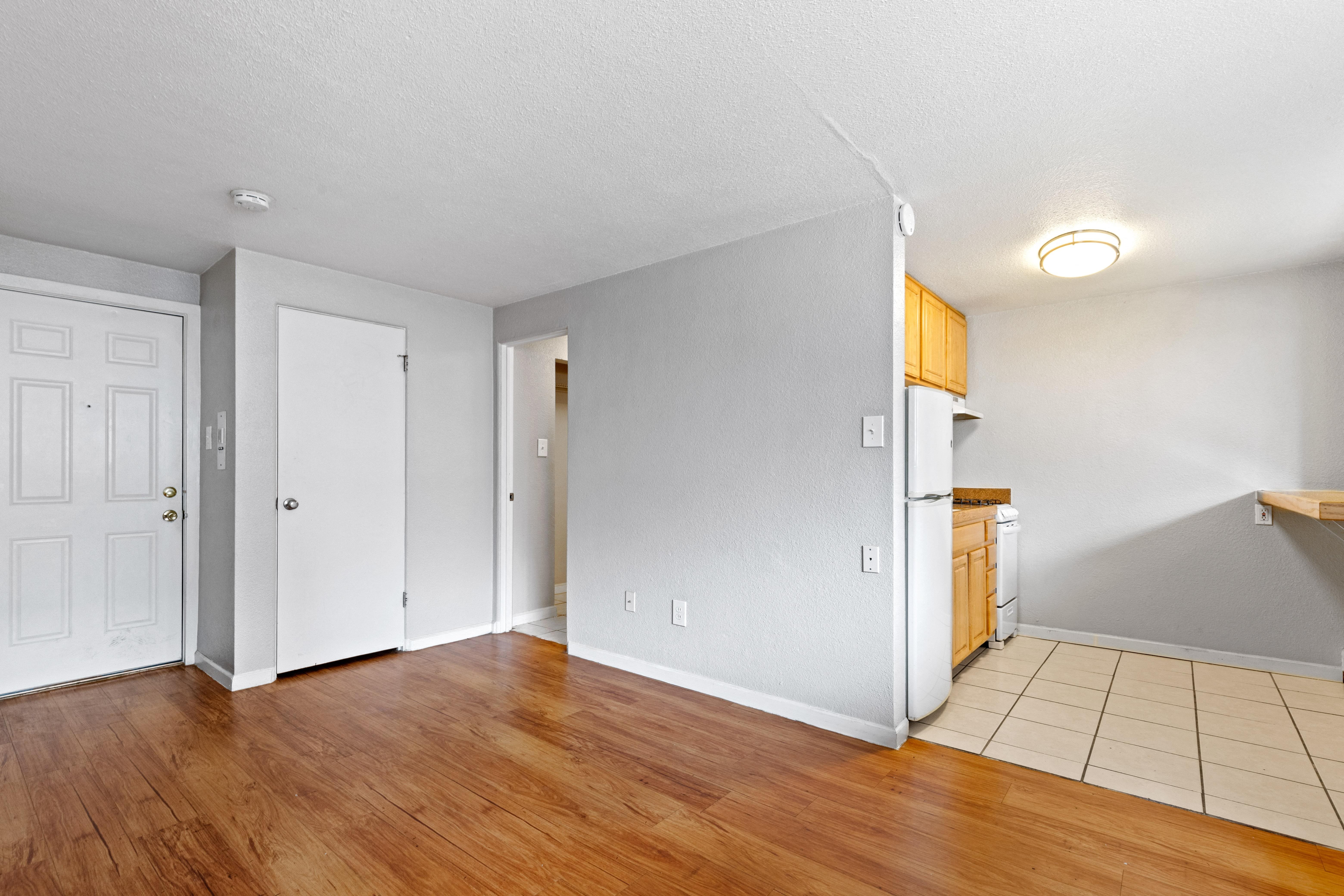 the living room and kitchen of an empty house with wood floors and white walls